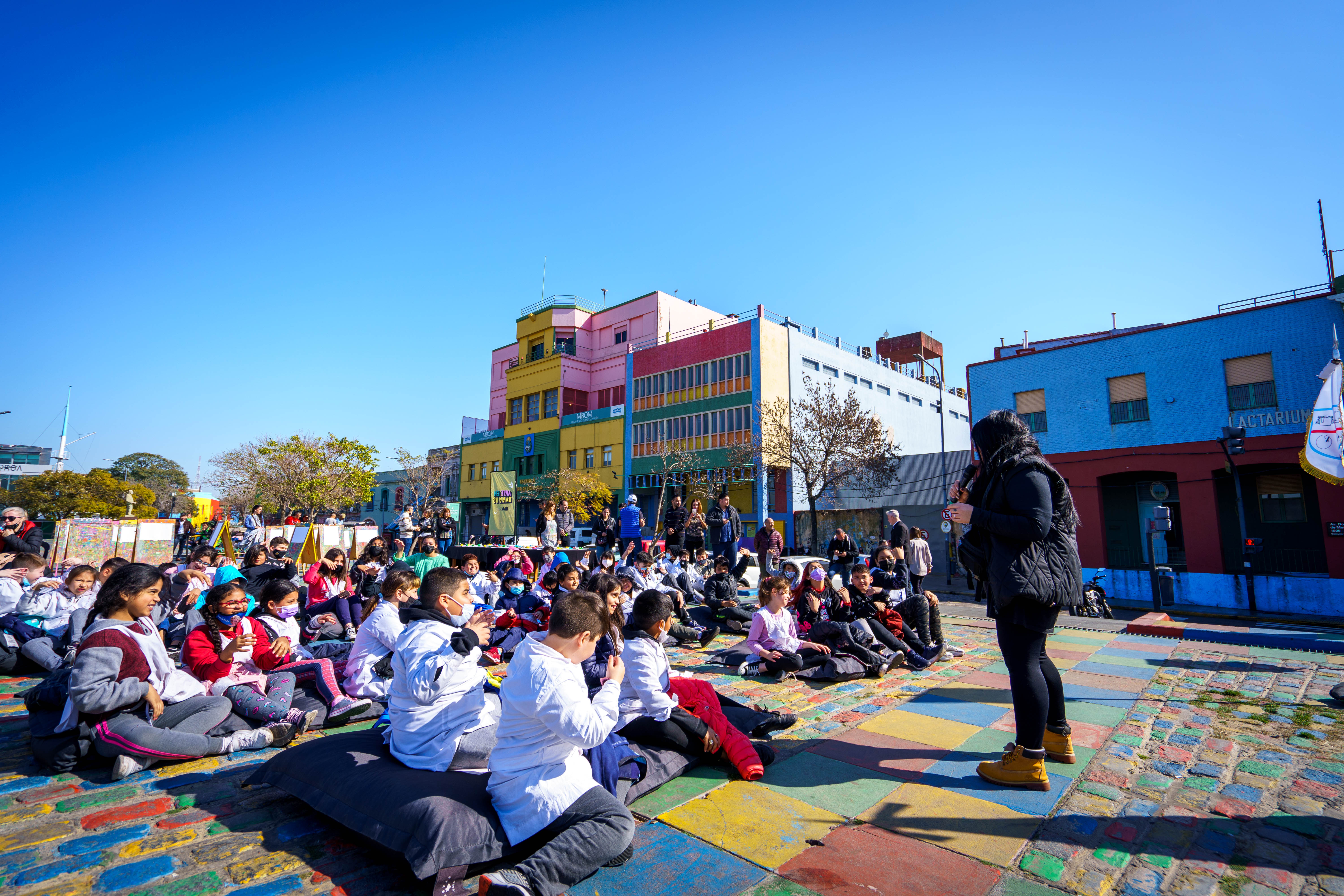 Niñas y niños de escuelas sentados en la vereda del Riachuelo de la Boca, frente al Museo Benito Quinquela Martin