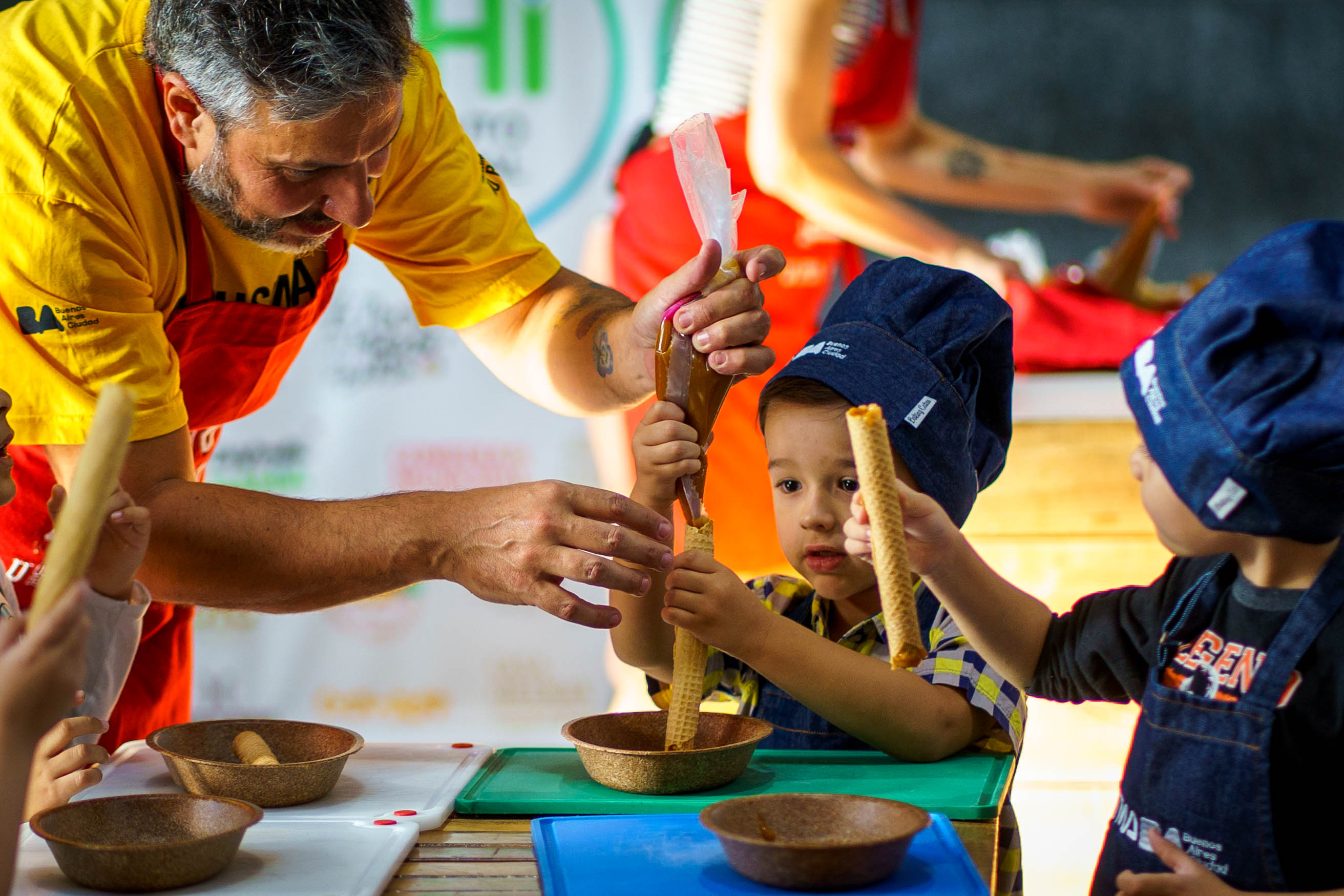 Dos niños rellenan cubanitos con dulce de leche junto a un adulto durante la actividad de Experimento Cocina en la Usina