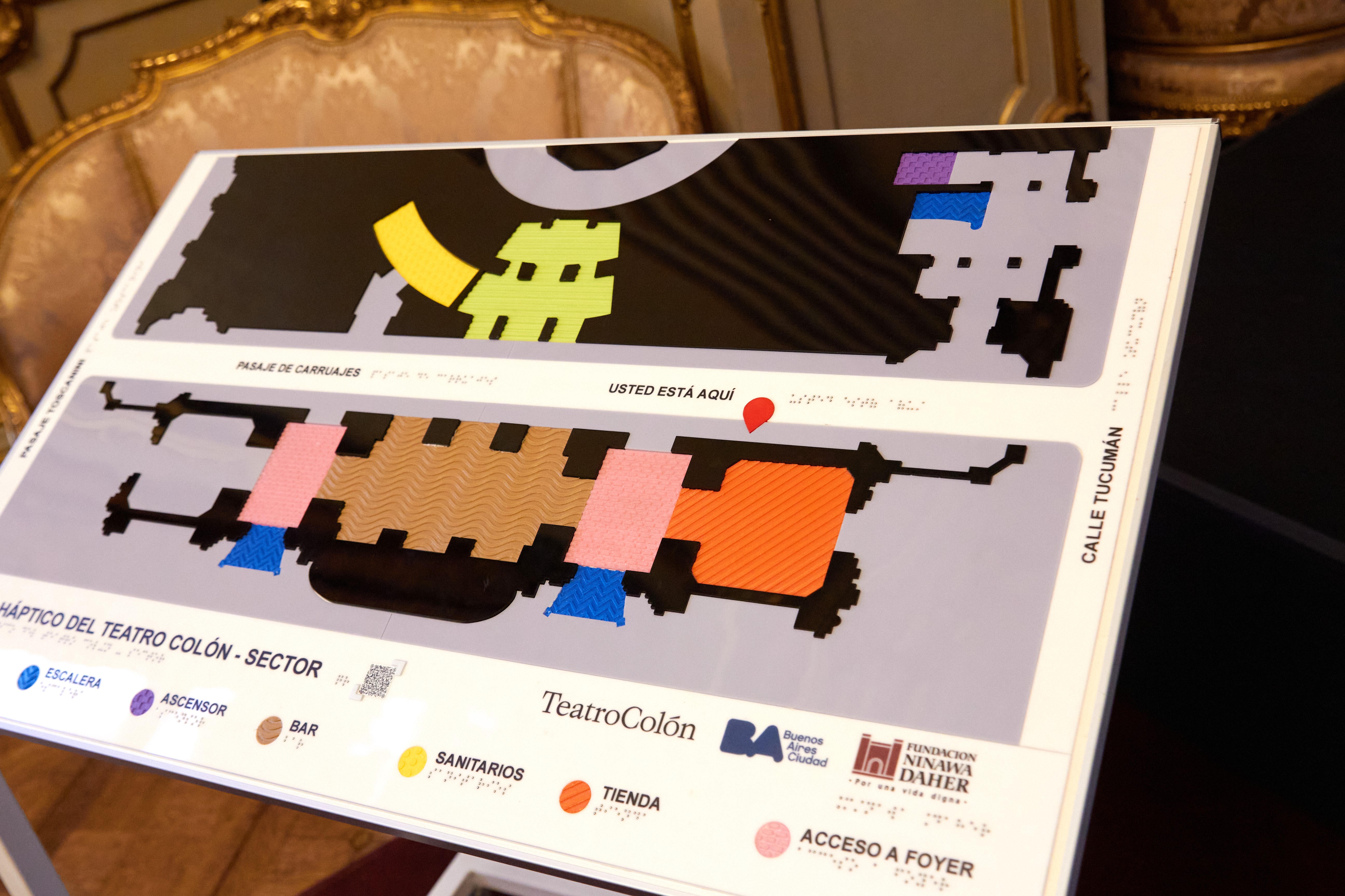 Detalle de un plano háptico del Teatro Colón que muestra sectores del edificio con texturas y colores accesibles, acompañado de leyendas en braille.
