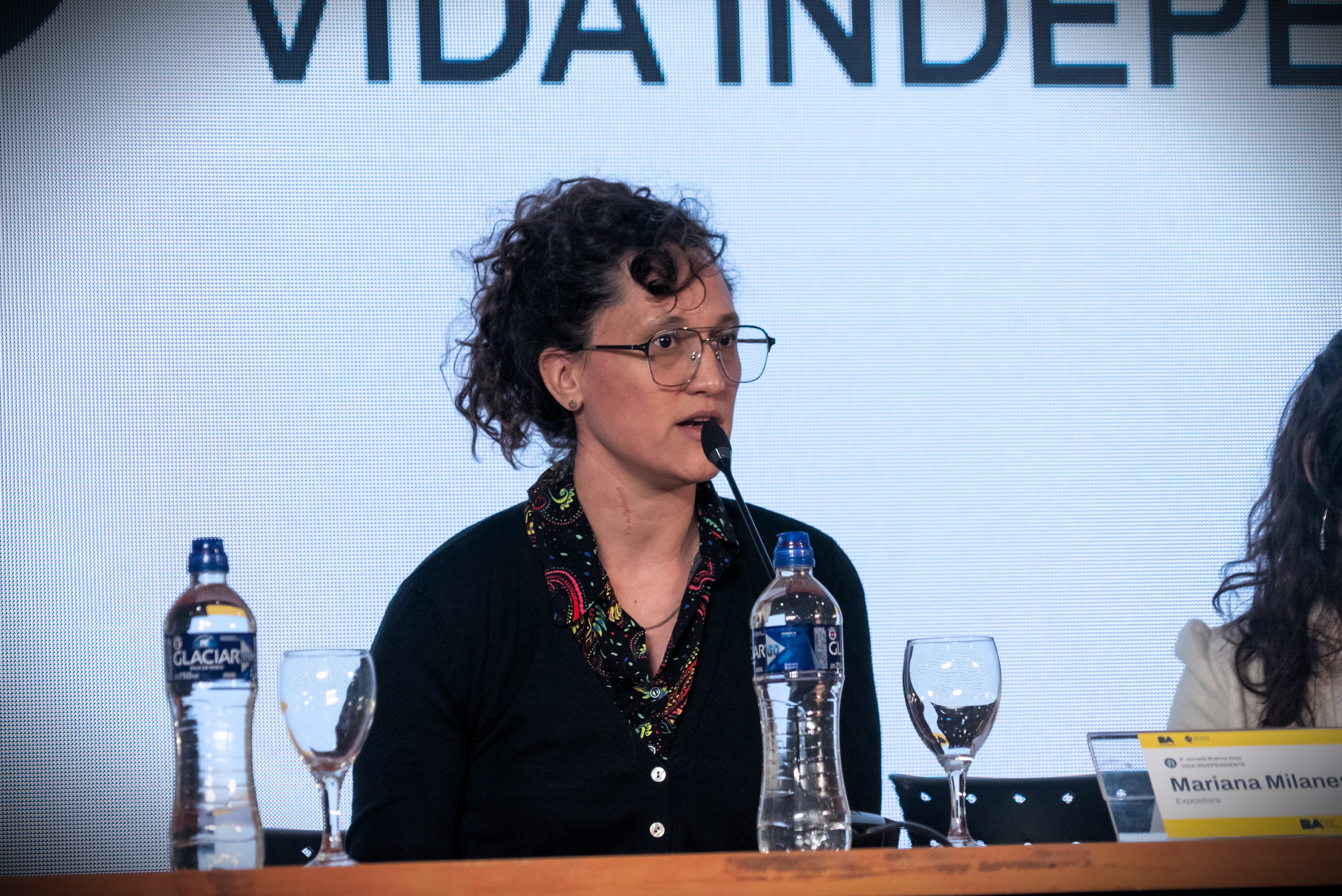 Imagen de Marianela Milanes en medio de su exposición. Frente a ella microfono, agua y copas