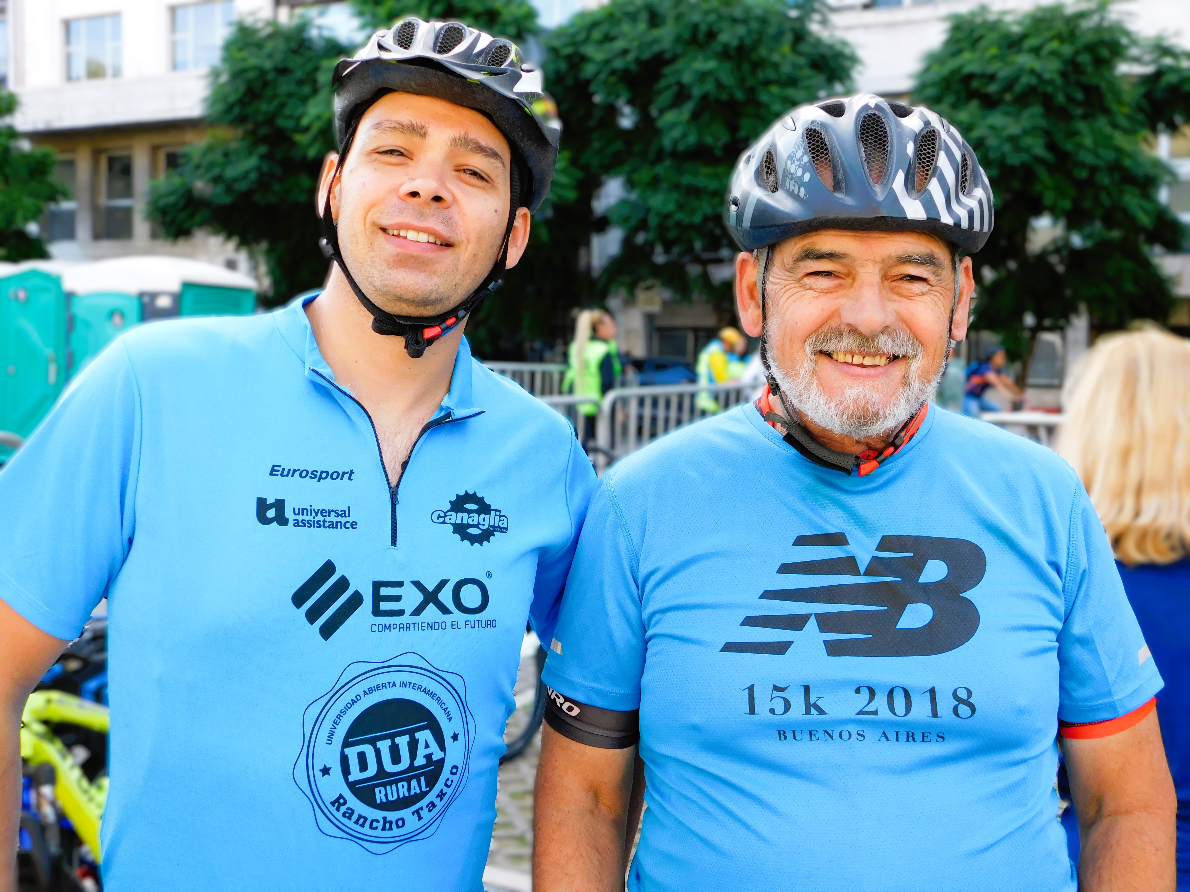 Fotografia de dos personas hombres con remeras de color azul y cascos de ciclitas mirando y sonriendo a cámara