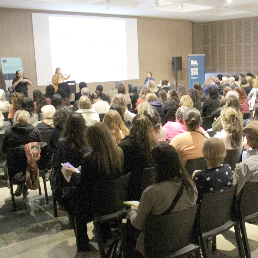 Auditorio del Museo lleno, con oradora e intérprete de Lengua de Señas Argentina en el escenario, sillas ordenadas y público atento.
