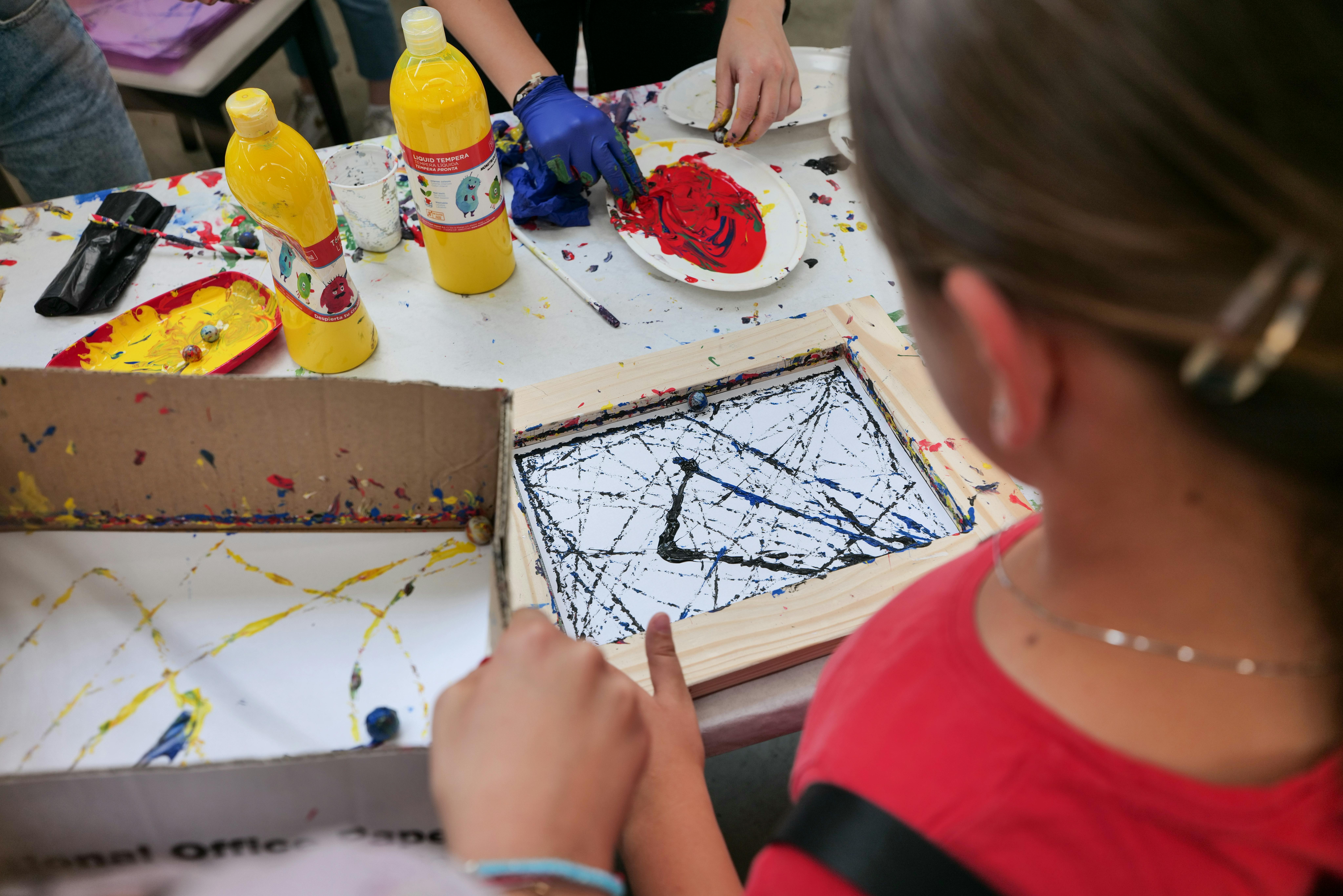 Fotografia en la que se observan a niños y niñas frente a una mesa de trabajo haciendo arte con pinturas
