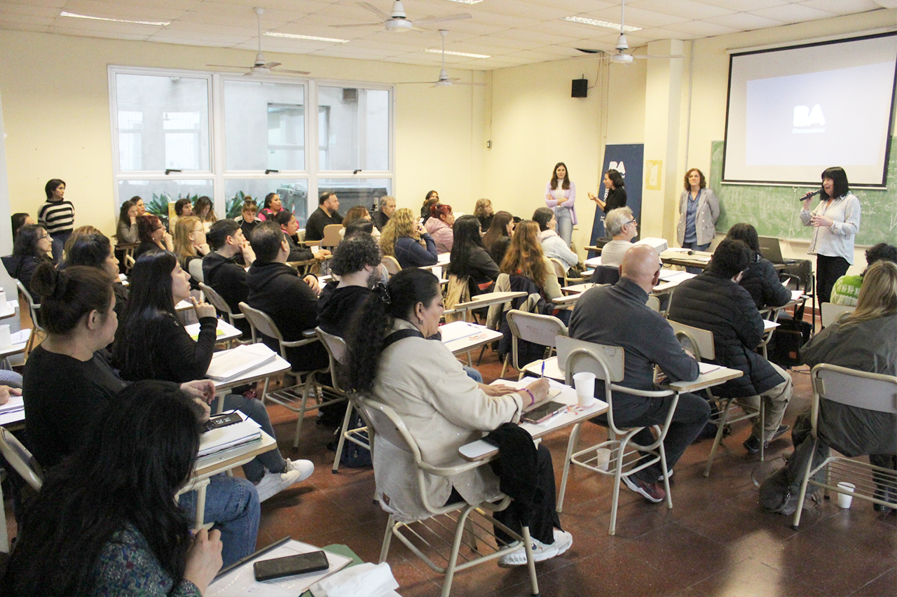 Personas participando de la capacitación en un aula universitaria, con una expositora hablando al frente.