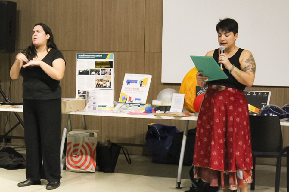 Una mujer intérprete de Lengua de Señas Argentina interpreta el documento que lee otra persona con micrófono en mano durante una actividad de capacitación.