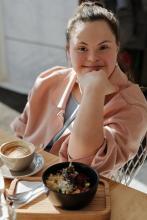 Una joven mujer en una mesa, con platos de comida y bebidas, compartiendo un momento de convivencia.