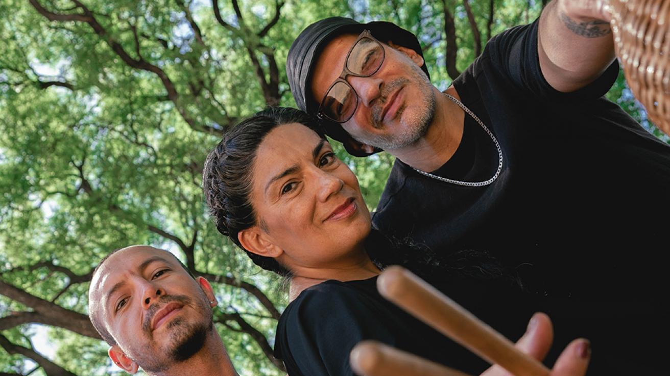 Los musicos Mariana Baraj, Leo Camargo y Marcelo Baraj posan con instrumentos sobre un fondo de arboleda verde