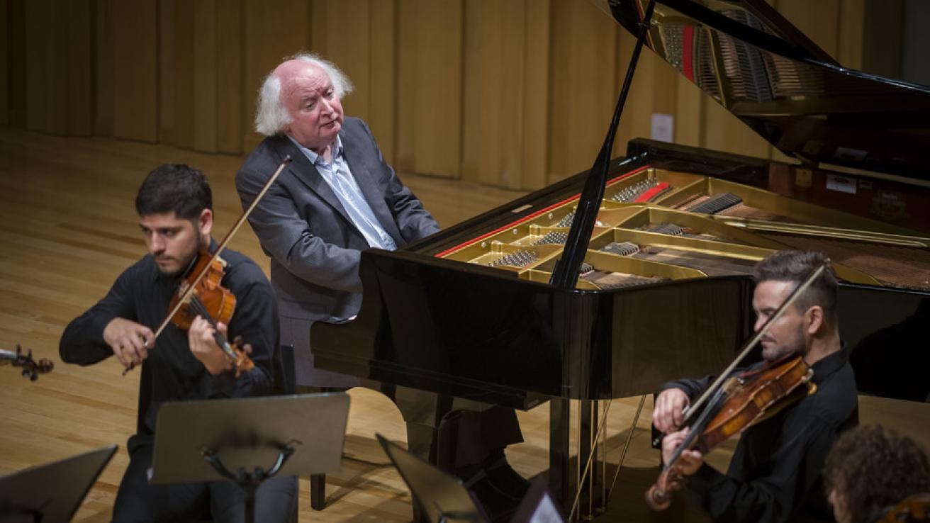 Miceal O'Rourke tocando el piano junto a 2 violinistas en escenario