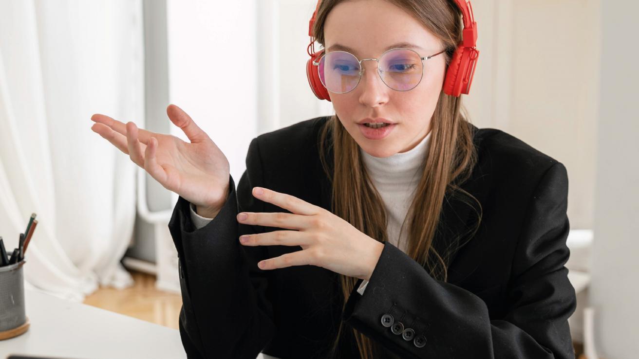 Mujer con auriculares rojos sentada en un escritorio con una computadora portátil.