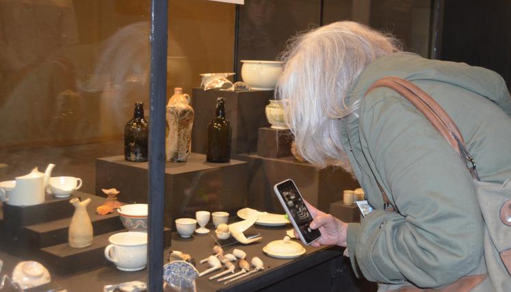 Mujer sacando una foto con el celular a una vitrina con piezas arqueologicas 