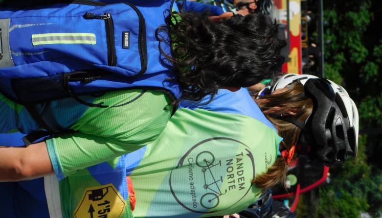 Fotografia de dos personas de espaldas donde se destaca en una de ellas remera cuyo texto dice:  tandem norte - ciclismo adaptado