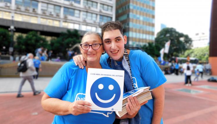 Madre e Hijo mirando a camara sonriendo y sosteniendo un cartel de una carita azul feliz