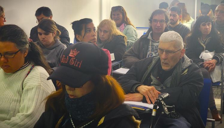 Una mujer en primer plano lleva una gorra negra con la inscripción "Bad Girl". La iluminación es suave, y el ambiente parece ser de aprendizaje. En el fondo, se pueden ver computadoras o dispositivos. 