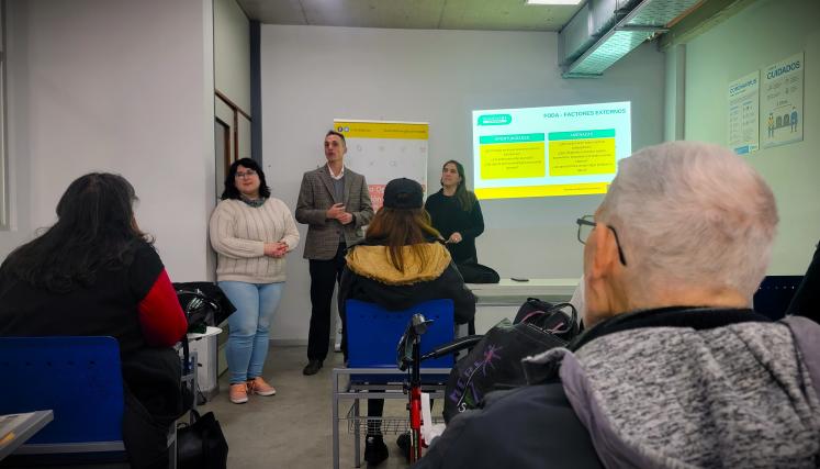 La imagen muestra a tres personas en un entorno de presentación, La capacitadora, Pedro Crespi y una integrante del equipo del Registro Laboral de COPIDIS, en el aula o sala de conferencias. En el centro, Pedro Crespi con un traje de cuadros está de pie, hablando y parece estar explicando algo a la audiencia. A su izquierda, hay una mujer con cabello rizado y gafas, que escucha atentamente. A la derecha, otra mujer con cabello largo y lacio también está prestando atención. Al fondo, se puede ver un cartel c