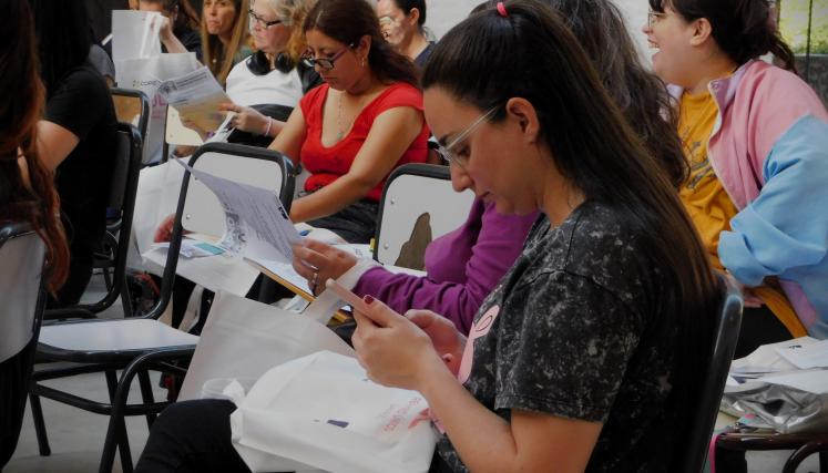 Imagen tomada en lateral de una parte del grupo presente. En su mayria mujeres sentdas leyendo el contenido del kit de regalo