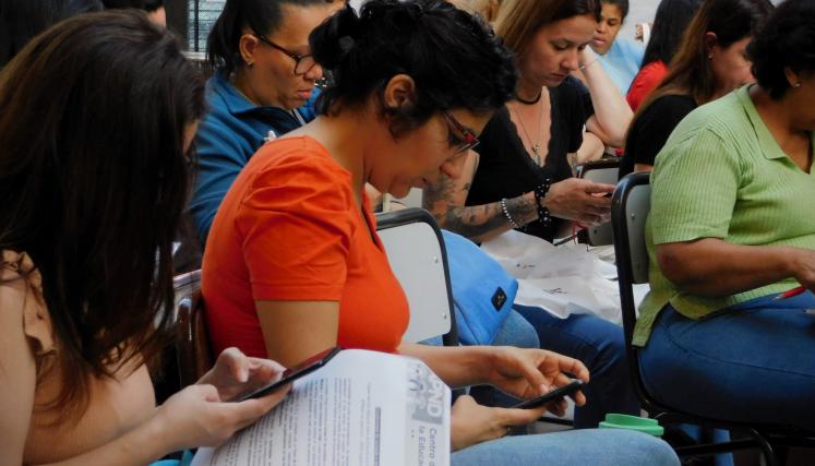 Imagen tomada en lateral de una parte del grupo presente. En su mayria mujeres sentdas leyendo el contenido del kit de regalo