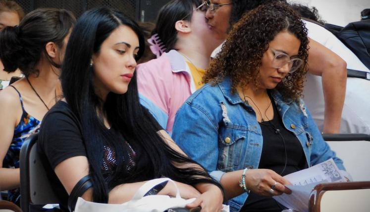 Imagen tomada en lateral de una parte del grupo presente. En su mayria mujeres sentdas leyendo el contenido del kit de regalo