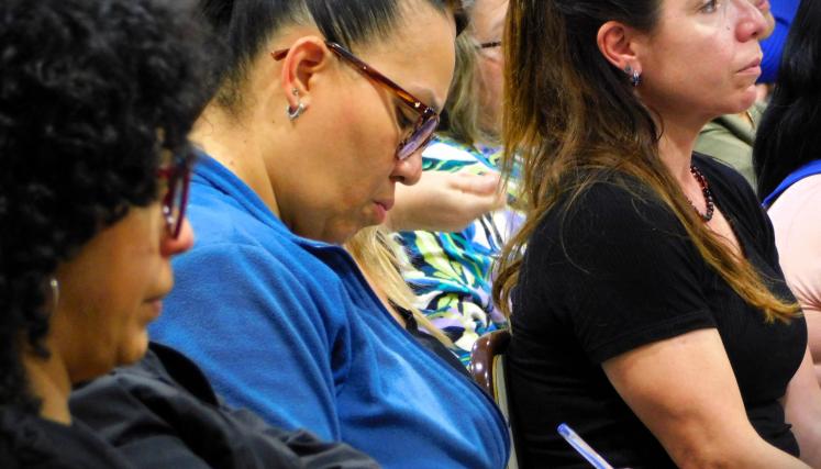 Imagen de un grupo de 3 mujeres sentadas. La del medio destaca por estar tomando apuntes con una lapicera