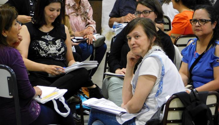 Fotografia tomada de un grupo de trabajo en la que la mayoria son mujeres. Una destaca por girar y mirar en atención lo que posiblemente son las palabras de un orador