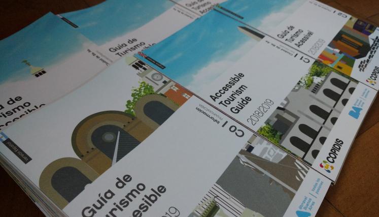 Tres folletos titulados: "guía de turismo accesible" con una ilustracion que representa varios edificios de la ciudad de Buenos Aires. Los folletos tienen un diseño en tonos Blanco, celeste y gris oscuro