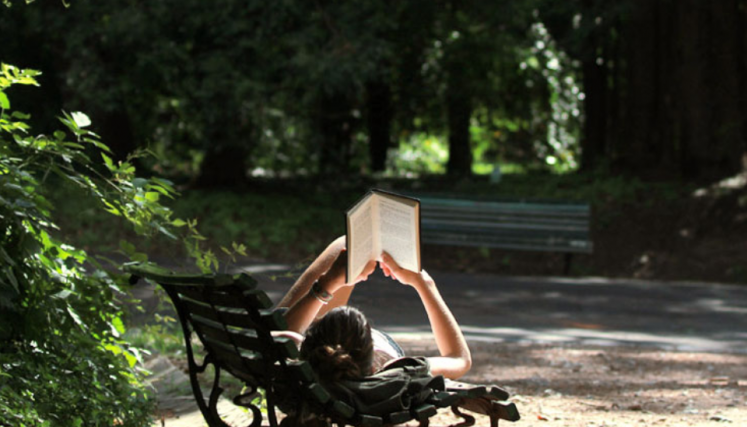 Persona leyendo acostada en un banco.