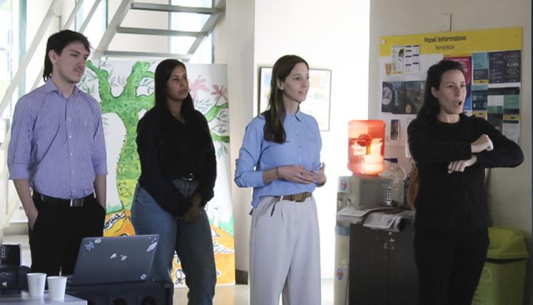 Equipo de cuatro personas exponiendo frente a un grupo; una intérprete de Lengua de Señas Argentina traduce la presentación