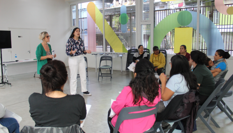 Dos oradoras frente a un grupo numeroso de personas que escuchan y están sentadas