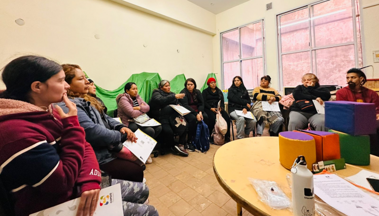 Grupo de personas sentadas en ronda participando de un taller sobre discapacidad. Algunas sostienen cuadernillos de COPIDIS y una persona está hablando. Se observan elementos de juego sobre una mesa en primer plano.