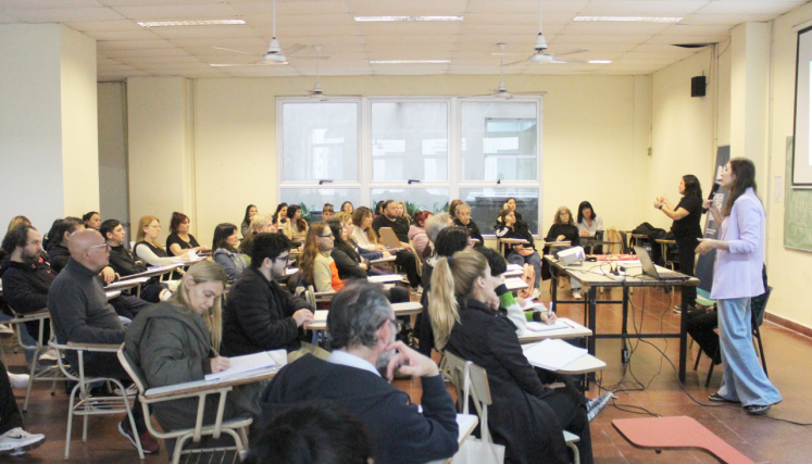 Charla en un aula con personas adultas sentadas y tomando nota, con la presencia de una intérprete de Lengua de Señas Argentina y una expositora. 