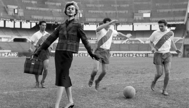 Mujer posando en cancha de futbol con hombres jugando a la pelota