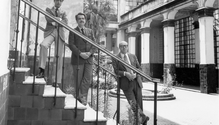 Tres hombres de traje en una escalera que da a un patio