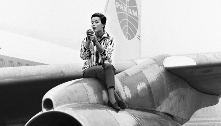 Mujer sentada sobre turbina de avión, pintándose los labios