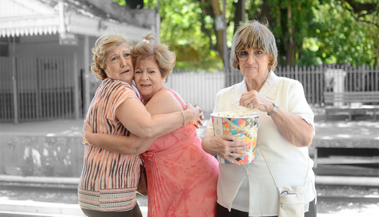 tres señoras de avanzada edad en la estación de tres. Dos están abrazadas, la otra comiendo pochoclo