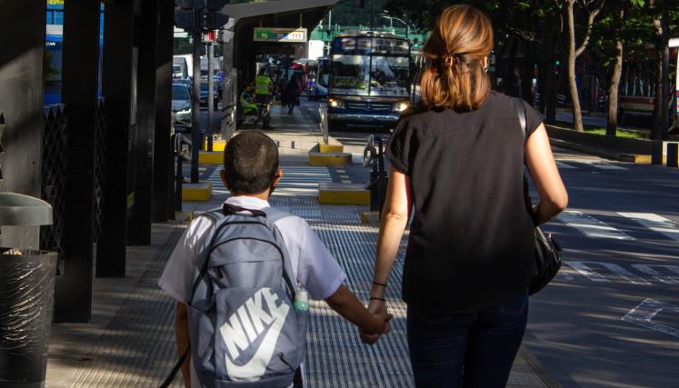 mujer y nene con guardapolvo blanco esperando el colectivo en el metrobus