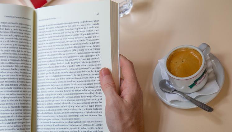 manos tomando un libro con una taza de cafe 